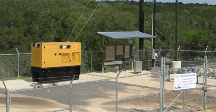 CAT standby generator beside solar-powered control panels at a fenced water well site