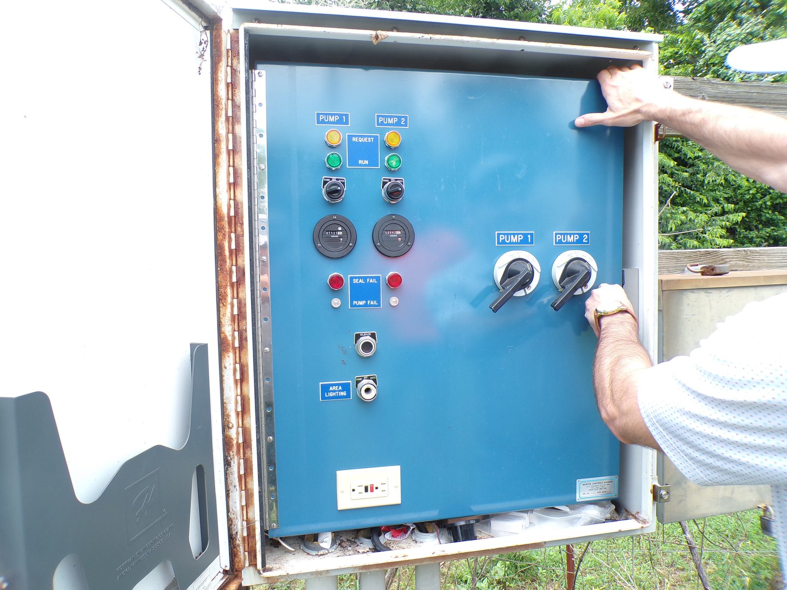 Weathered outdoor duplex pump control panel with hand-off-auto selector switches, elapsed time meters and seal fail alarms, still in service
