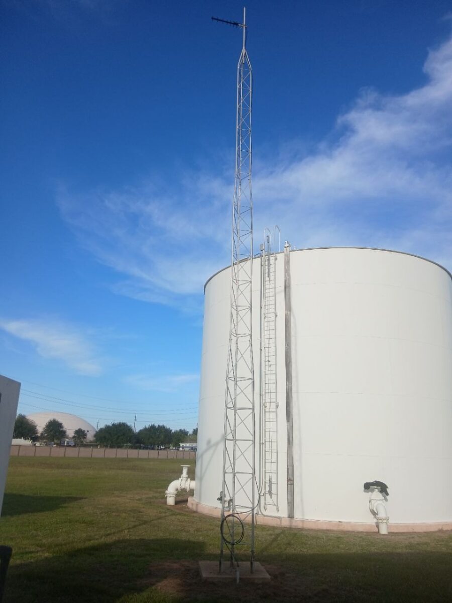 Ground storage tank with telemetry antenna mast against a clear Texas sky